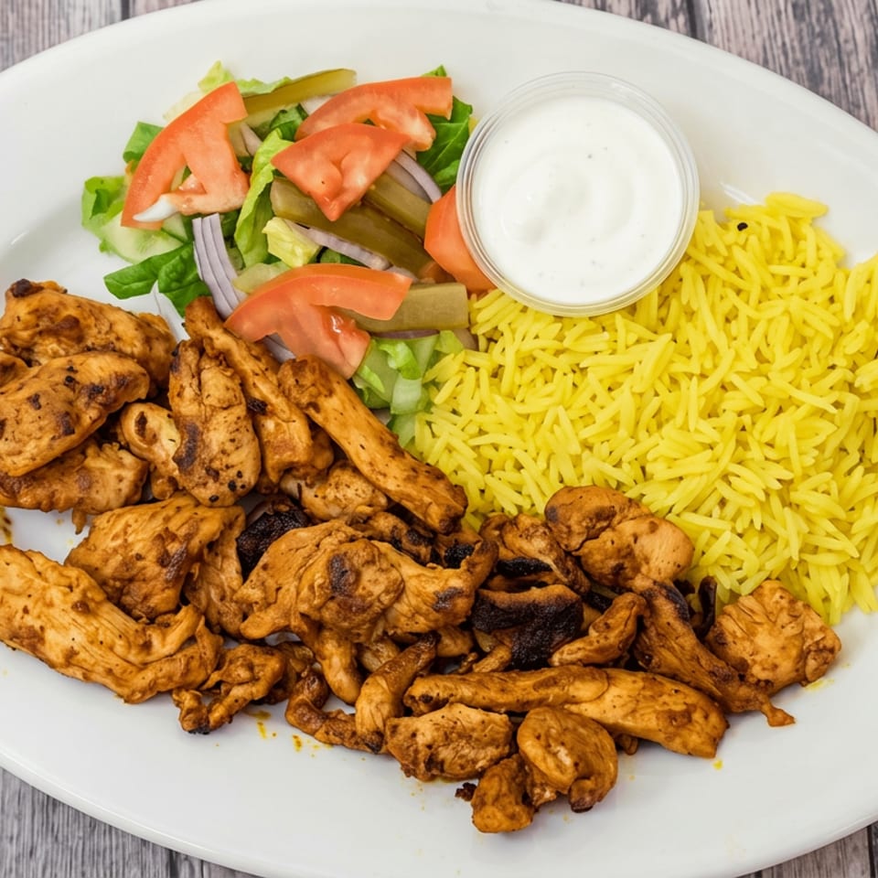 Plate of grilled spiced chicken with yellow rice, green salad, tomato, onions, pickles, and creamy dipping sauce.