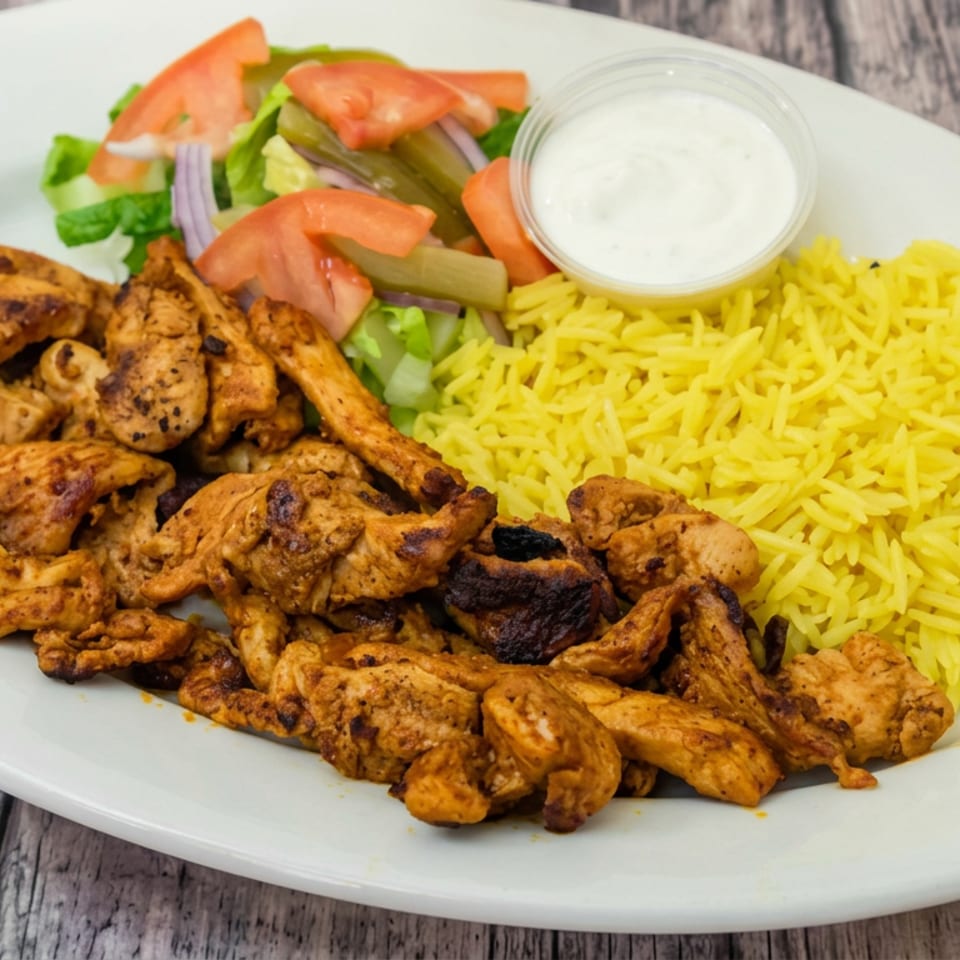 Grilled seasoned chicken pieces with yellow rice, salad, pickled vegetables, and creamy sauce on a white plate.