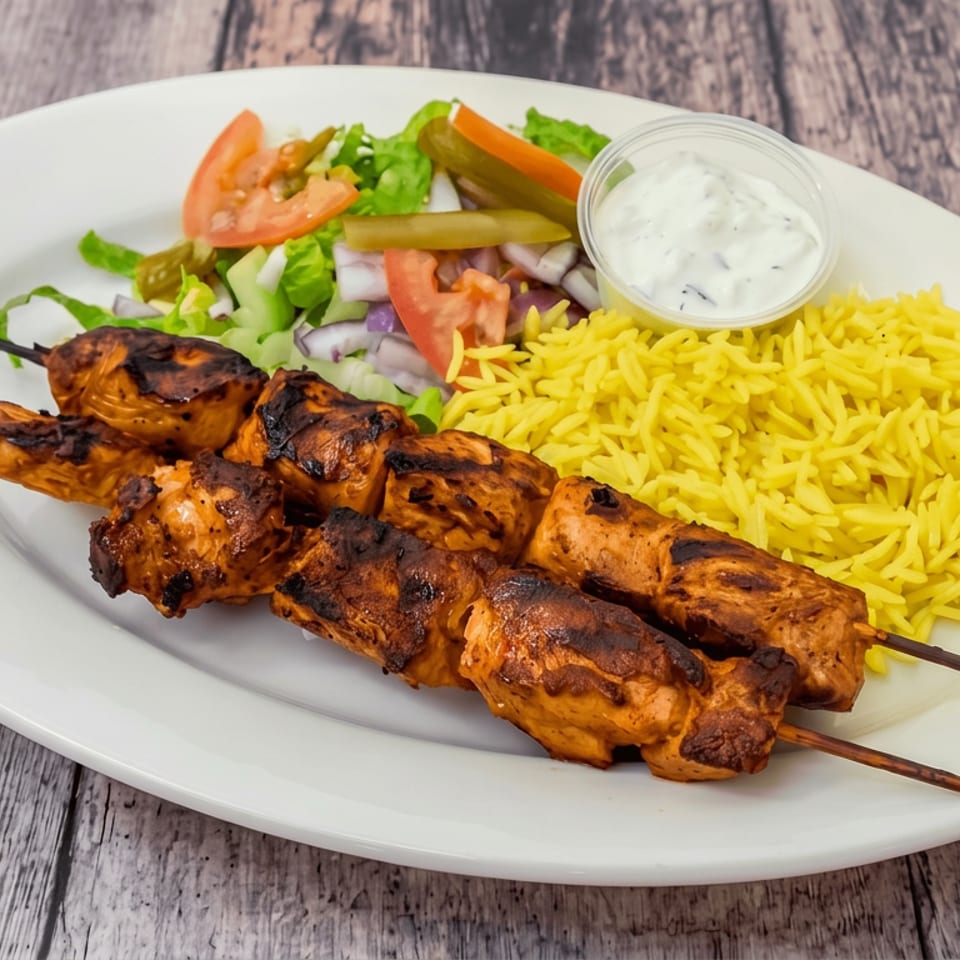 Grilled chicken skewers with yellow rice, salad, pickled vegetables, and creamy dipping sauce on a white plate.